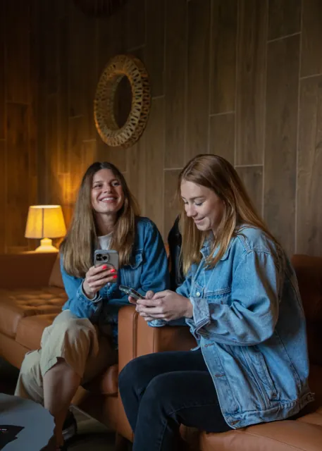 Two guests sitting on a sofa with their phones