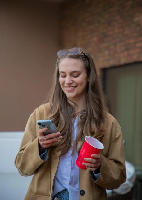 A guest smiling at her phone, drink in hand